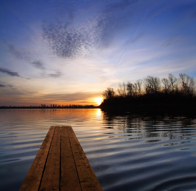 Paisaje fluvial con muelle y puesta de sol en el río.