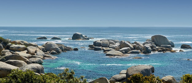 Paisaje de grandes rocas en el océano en verano Muchas piedras junto a la amplia playa vacía Rocas lisas o acantilados junto a la playa con olas ligeras y espumosas en la superficie Hout Bay Ciudad del Cabo Sudáfrica