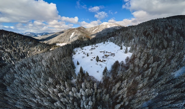 Paisaje invernal aéreo con pequeñas casas rurales entre bosques cubiertos de nieve en montañas frías.