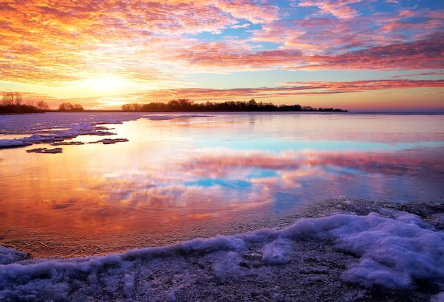 Paisaje invernal con lago y cielo ardiente al atardecer. Composición de la naturaleza.