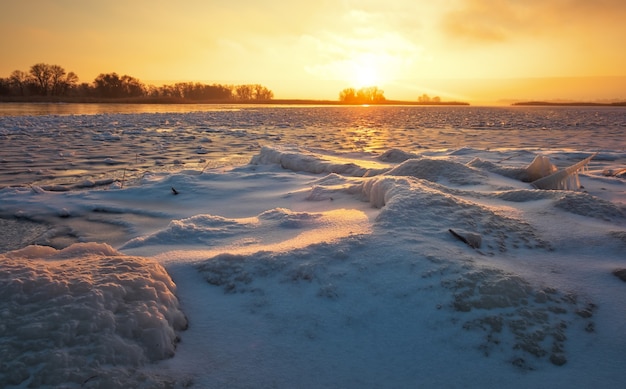 Paisaje invernal con lago congelado y cielo ardiente al atardecer. Composición de la naturaleza.
