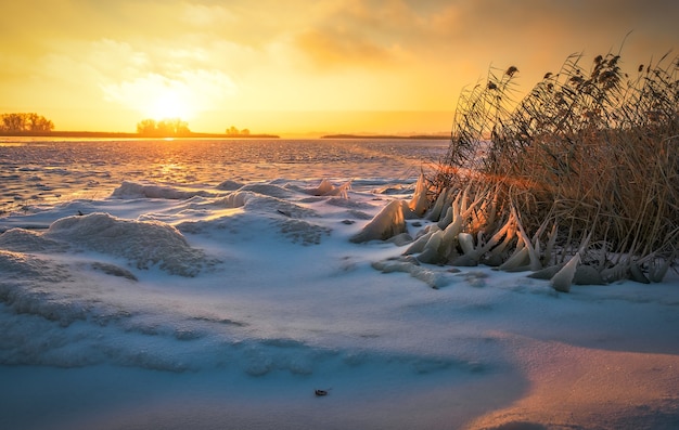 Paisaje invernal con lago congelado y cielo ardiente al atardecer. Composición de la naturaleza.