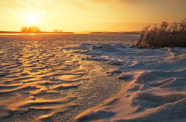 Paisaje invernal con lago congelado y cielo ardiente al atardecer. Composición de la naturaleza.