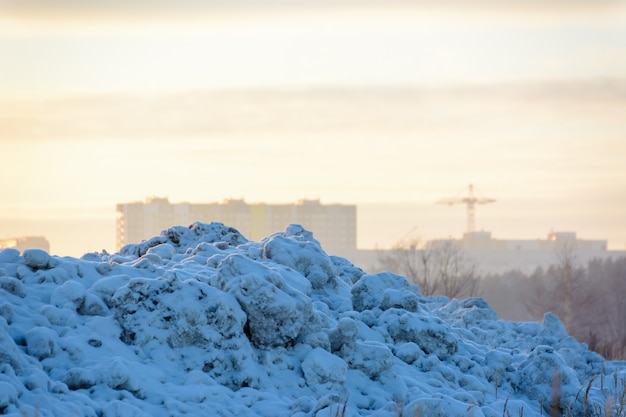 Foto paisaje invernal una montaña de nieve con el telón de fondo de un paisaje urbano al atardecer y una grúa torre