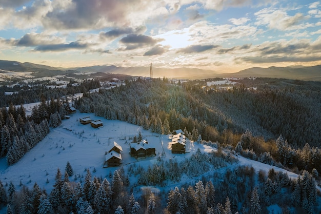 Paisaje de invierno aéreo con pequeñas casas de pueblo entre bosques cubiertos de nieve en las frías montañas de la noche.