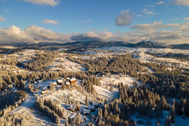 Paisaje de invierno aéreo con pequeñas casas de pueblo entre bosques cubiertos de nieve en las frías montañas de la noche.