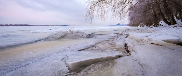 Paisaje de invierno al amanecer, orilla del río de un hielo congelado.