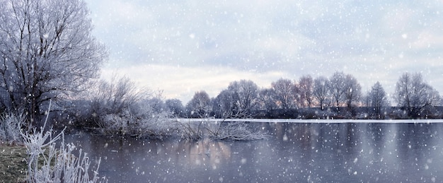 Paisaje de invierno atmosférico con río, árboles en la orilla, cielo nublado durante las nevadas. Nevadas en el rio