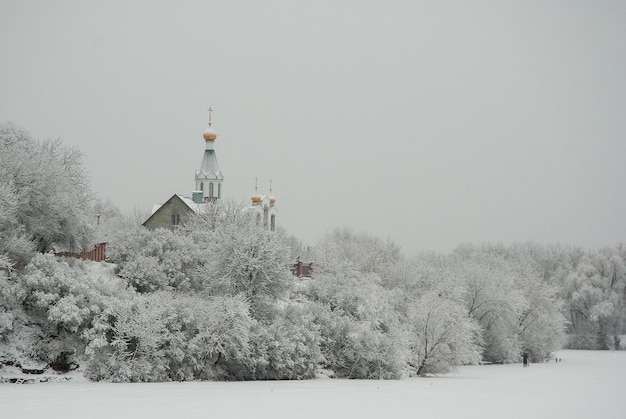 Foto paisaje de invierno en un lago congelado nieve blanca en los árboles y una iglesia en la orilla