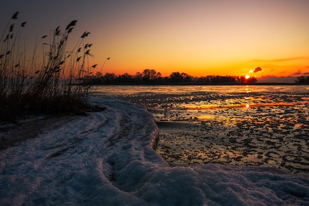 Paisaje de invierno natural en la orilla del mar durante la puesta de sol. Cielo de hielo y puesta de sol.