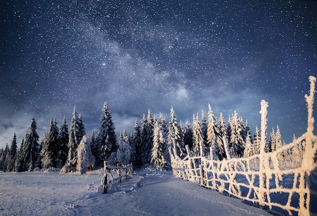 Paisaje de invierno. Pueblo de montaña en los Cárpatos ucranianos. Cielo nocturno vibrante con estrellas y nebulosas y galaxias. Astrofotografía de cielo profundo.