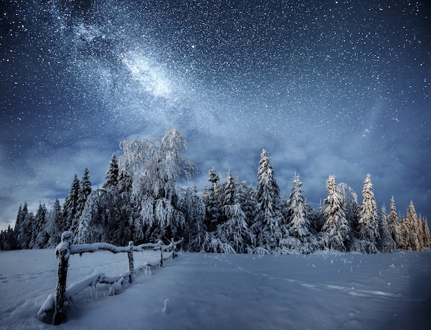 Paisaje de invierno. Pueblo de montaña en los Cárpatos ucranianos. Cielo nocturno vibrante con estrellas y nebulosas y galaxias. Astrofotografía de cielo profundo.