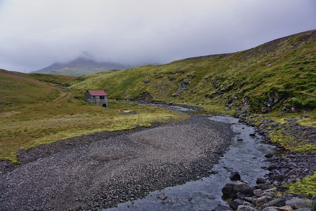 Paisaje islandés durante un día nublado. Un camino de ripio cerca de una casita en medio del campo.