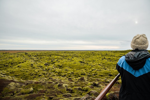 Foto paisaje islandés de un hombre desde atrás mirando hacia una formación rocosa con musgo verde