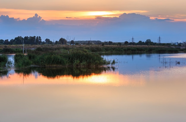 Paisaje de lago de verano al atardecer con reflejo de sol en la superficie del agua (cerca del asentamiento de Shklo, Óblast de Lviv, Ucrania).