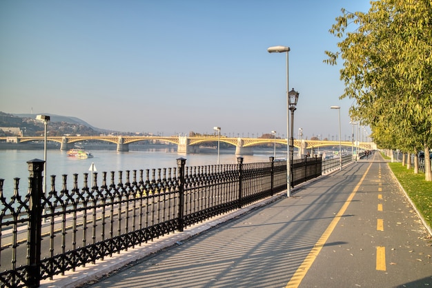 Paisaje de la mañana con vistas a la acera a lo largo del río Danubio con vistas al Puente Margarita en Budapest, Hungría, sobre un fondo de cielo azul claro.