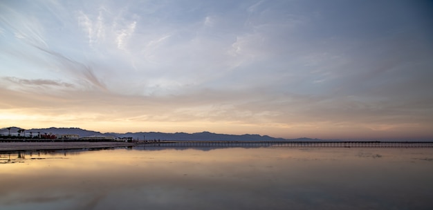 Un paisaje de mar con un largo muelle y montañas en el horizonte.