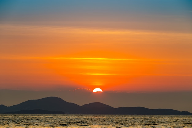 Paisaje de mar con puesta de sol detrás de montaña y mar