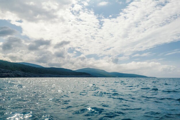 Paisaje de mar, superficie del agua, cielo nublado y montañas