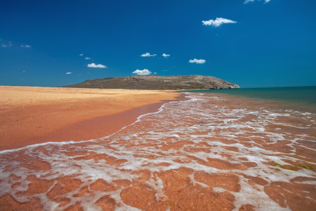 Foto paisaje marino en un día soleado playa de arena con cielo azul y monte en el horizonte