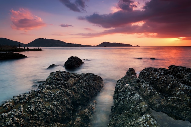 Paisaje marino dramático del cielo con la roca en fondo del paisaje de la puesta del sol.