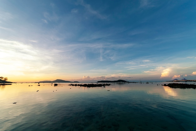 Paisaje marino dramático del cielo con la roca en el paisaje de la salida del sol y la reflexión hermosa en el mar