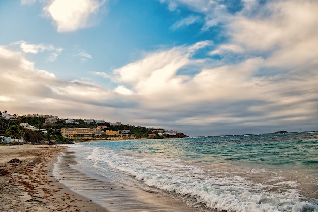 Paisaje marino con olas del mar o del océano, playa de arena y ciudad turística sobre fondo de cielo azul nublado en Philipsburg, Sint Maarten. Vacaciones de verano y viajes. Concepto de recreación y relajación.