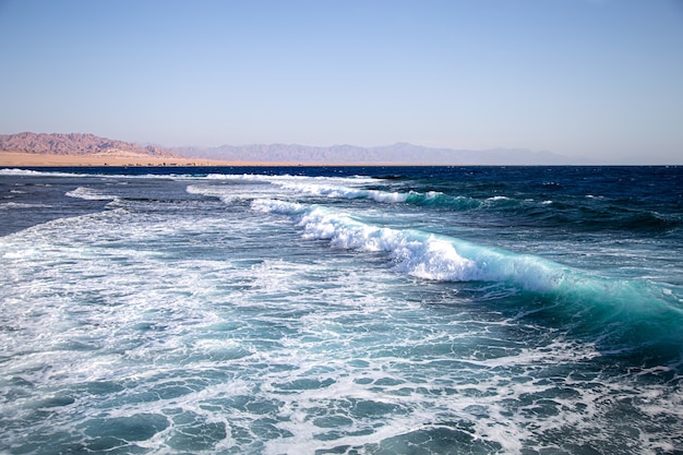 Paisaje marino con olas con textura y siluetas de montaña en el horizonte.