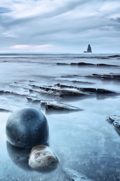 Paisaje marino de rocas y mar al atardecer. Una piedra redonda en primer plano.