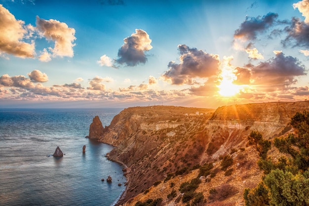 El paisaje marino sobre la playa durante la puesta de sol con un acantilado rocoso está iluminado por la cálida exposición prolongada de la puesta de sol