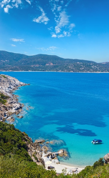 Paisaje marino de verano con barco en agua transparente color aguamarina y playa de arena en la costa rocosa Vista desde la costa Sithonia Halkidiki Grecia