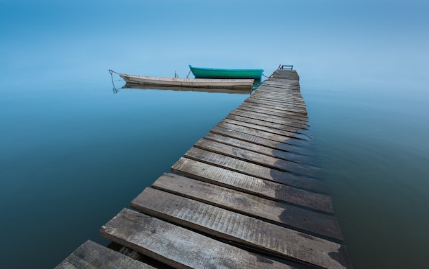 Foto paisaje meditativo con viejo muelle de madera y barcos de madera, larga exposición, horizonte infinito