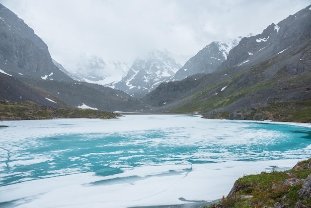 Foto paisaje de montaña atmosférico con lago alpino congelado durante las nevadas paisaje frío impresionante con nevadas en valles de alta montaña con lago de montaña helado en el fondo de montañas de nieve en nubes bajas
