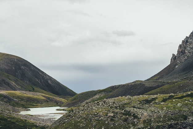 Paisaje de montaña atmosférico con lago de montaña cerca de rocas afiladas en un valle estrecho en tiempo lluvioso