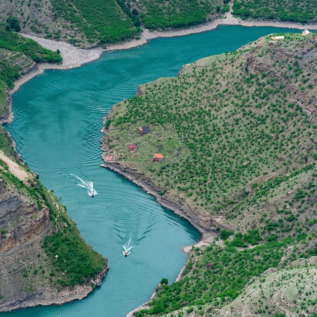 Paisaje de montaña con un cañón profundo con un río azul a lo largo del cual se mueve un bote a motor