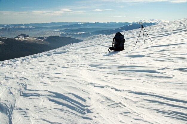 Paisaje de montaña invernal con mochila turística y trípode fotográfico