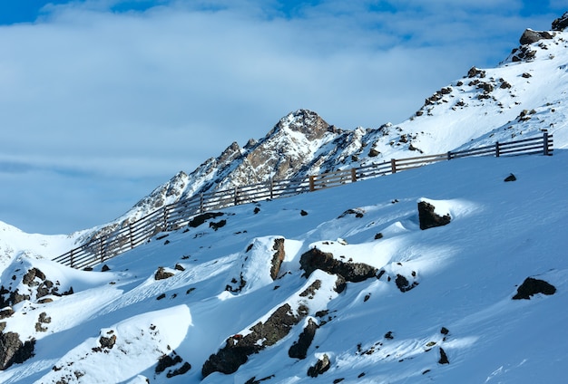 Paisaje de montaña de invierno por la mañana con valla de madera a lo largo de la pista de esquí.