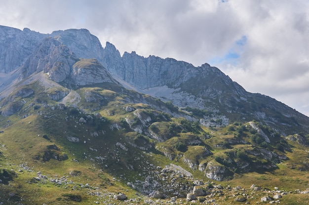 Foto paisaje de montaña: una ladera con cornisas verdes, y sobre ella un pico rocoso inexpugnable