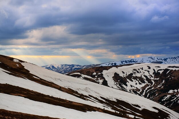 Paisaje de montaña de primavera con nieve y hierba Nubes dramáticas en el horizonte y el sol brilla Fondo natural de viaje al aire libre en estilo retro hipster