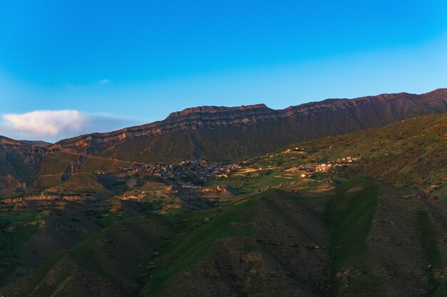 Paisaje de montaña con un pueblo en una ladera bajo una enorme cresta rocosa Chokh en Daguestán