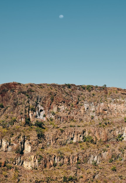 Un paisaje de montaña rocosa con la luna en el cielo azul.