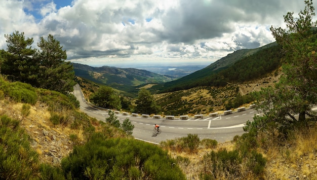 Paisaje de montaña verde con una carretera y ciclistas bajando.