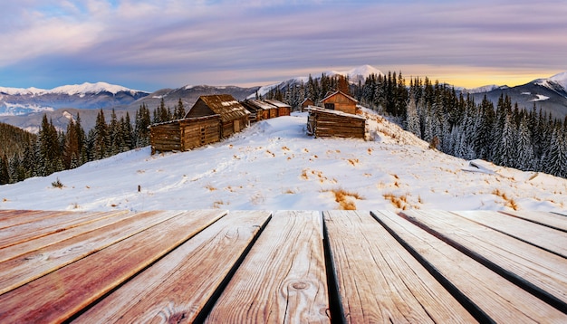 paisaje de montañas de invierno con un bosque nevado y una cabaña de madera y mesa en mal estado.