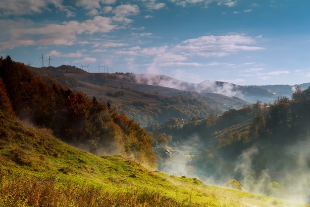 Paisaje montañoso del otoño cubierto en la niebla persistente de la niebla con la luz caliente de la mañana.