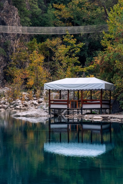 paisaje montañoso vertical de otoño con lago sombreado, cenador de picnic y puente colgante