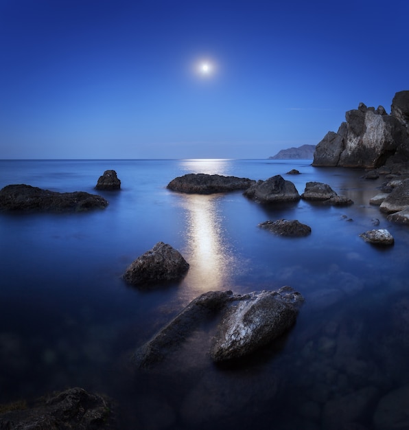 Paisaje nocturno con luna llena, camino lunar y rocas en verano