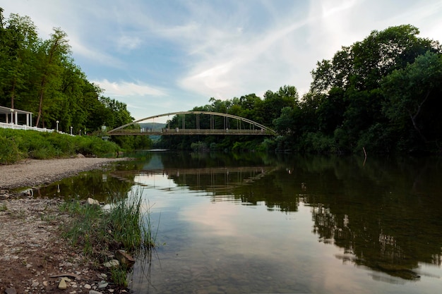 Paisaje en la orilla del río con un puente y un reflejo del cielo al atardecer...