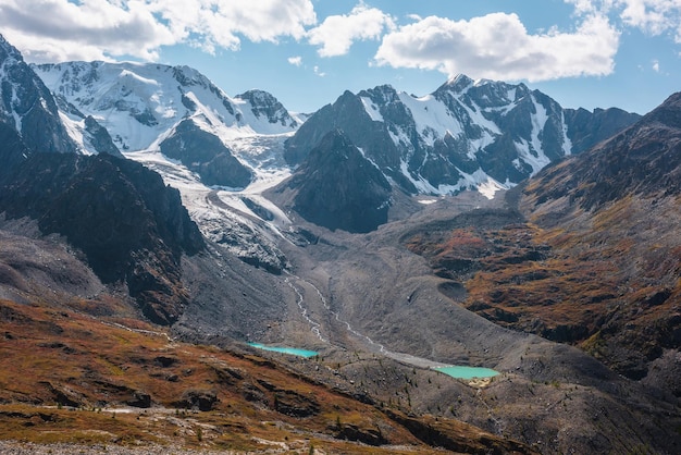 Paisaje otoñal variopinto con dos pequeños lagos en un valle alto y una gran cadena montañosa nevada con glaciar en un día soleado Colores otoñales vivos en las montañas Lagos glaciales y paredes de montaña bajo un sol brillante