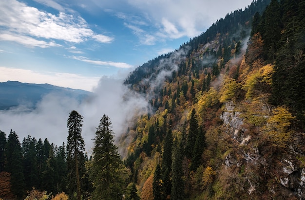 El paisaje de otoño de montaña con bosque colorido y altas cumbres de las montañas del Cáucaso. Estación de esquí de Rosa Khutor en temporada baja, Rusia, Sochi. Danza de las nubes de montaña