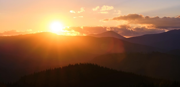 Paisaje panorámico de la hermosa noche con un brillante sol poniente sobre los picos de las montañas distantes al atardecer.